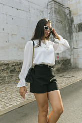 a lady in a white bow tie neck shirt and a pair of black shorts